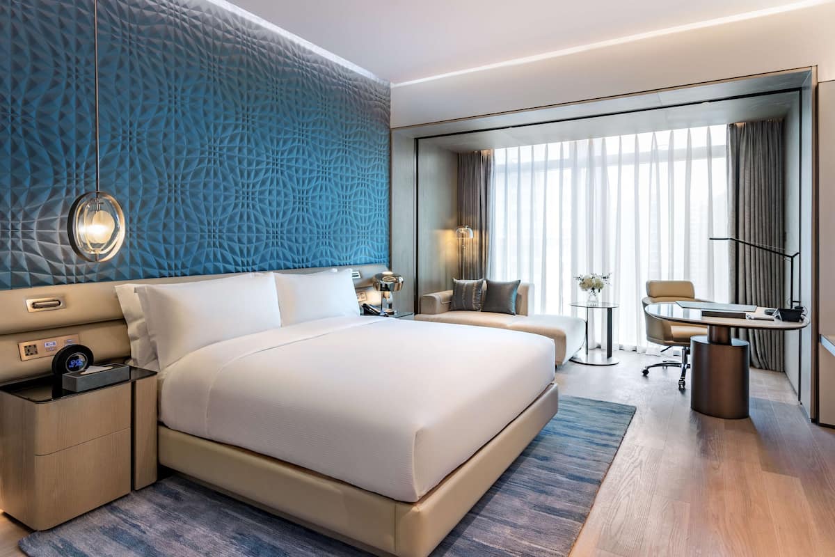 A modern hotel room with a large bed, a desk, and a seating area.