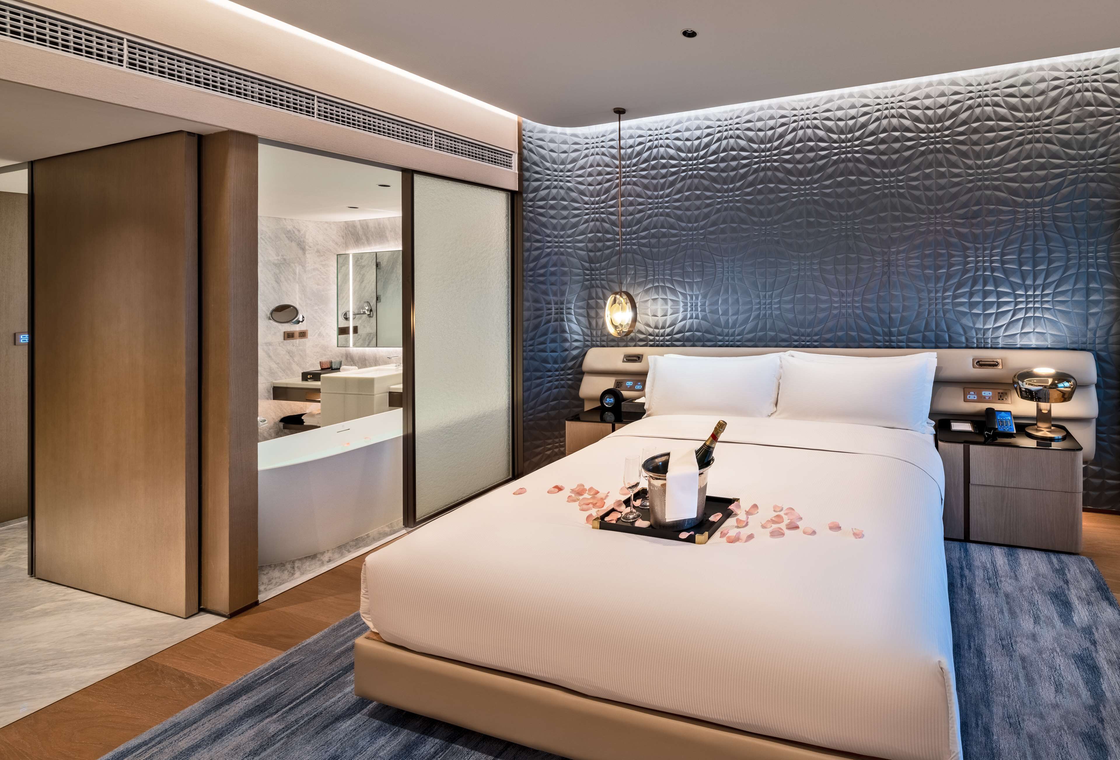 A modern hotel room with a large bed, a built-in vanity, and a unique textured wall.
