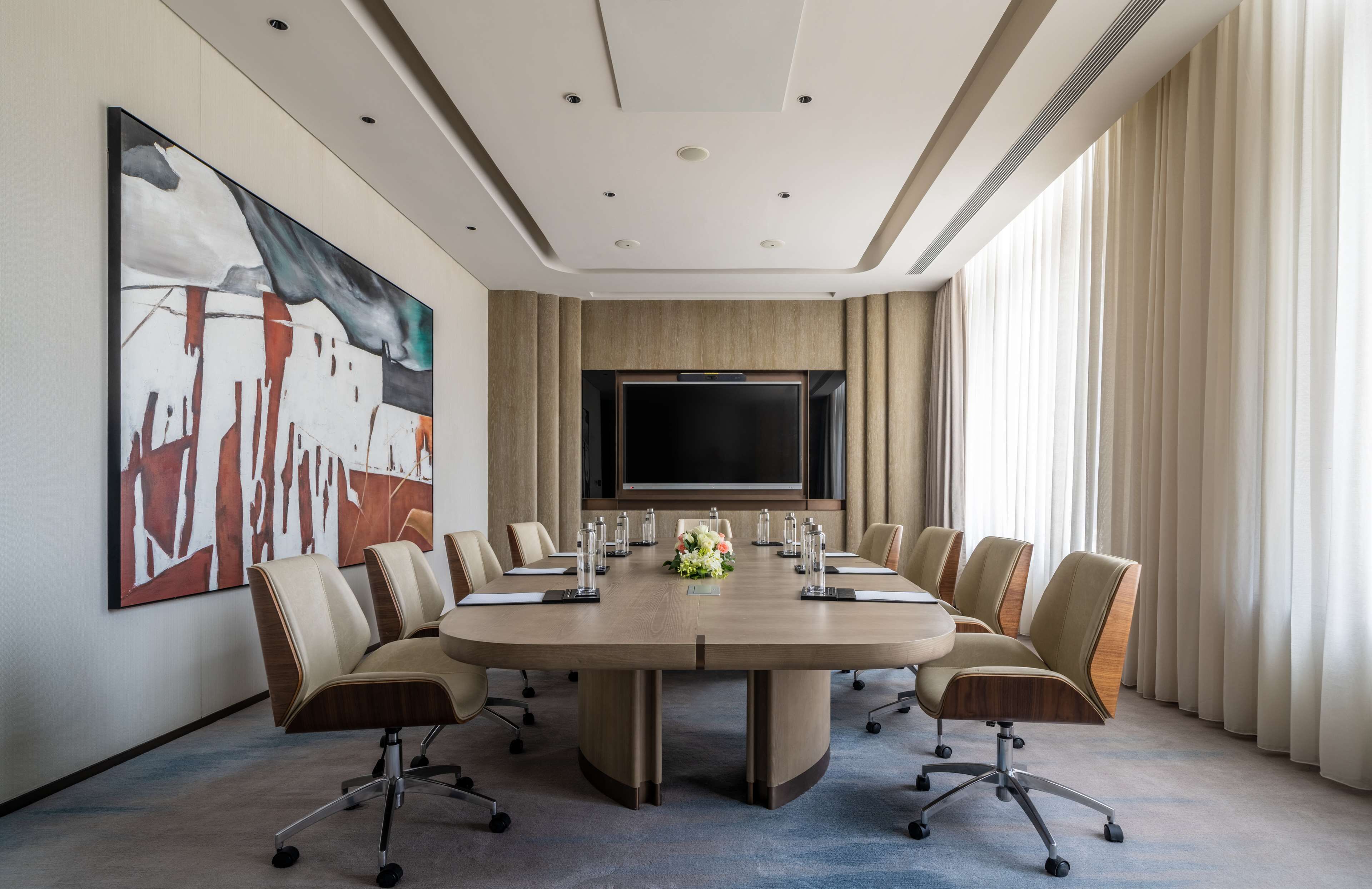 A conference room with a large table, chairs, a flat-screen TV, and a large abstract painting on the wall.