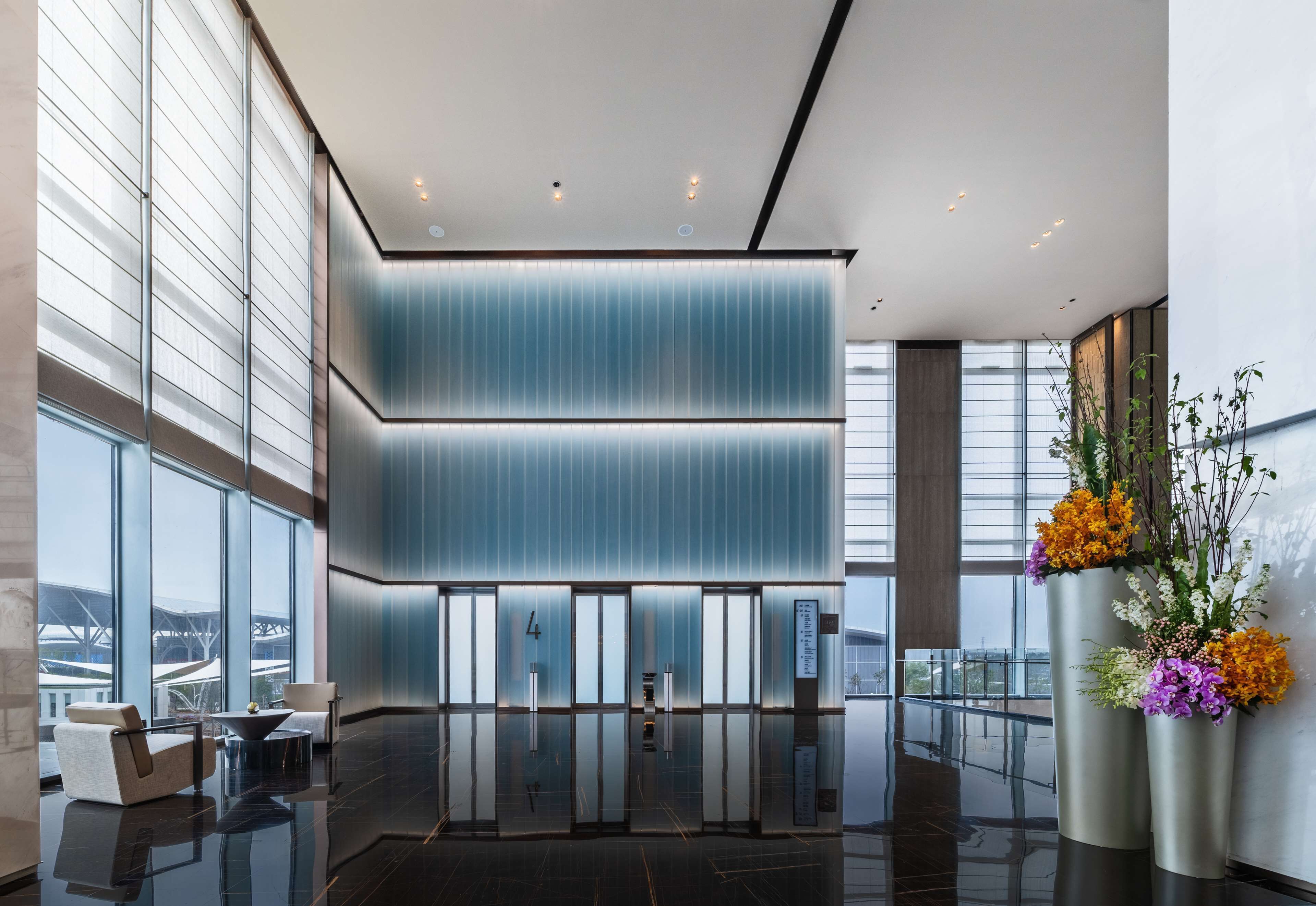 Un vestíbulo moderno con ventanas amplias, un mostrador de recepción y una decoración floral.