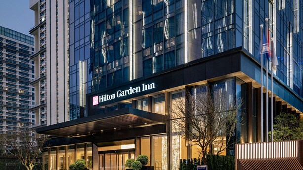 Een modern Hilton Garden Inn hotel met een opvallende ingang, grote ramen en een goed verlichte gevel.