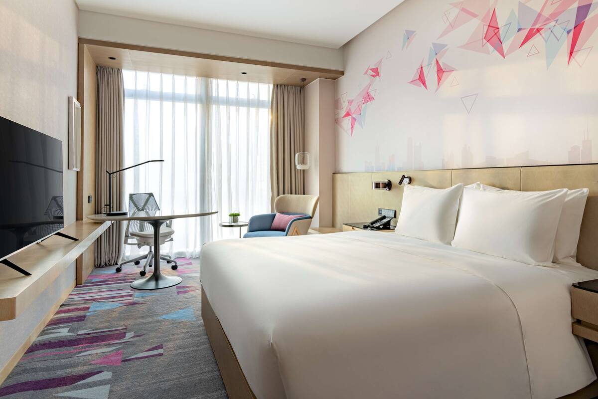 Een hotelkamer met een groot bed, een bureau met een stoel, een televisie en stadsgezicht kunst aan de muur.