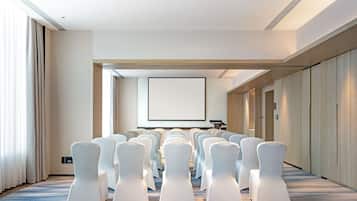 Un salón de conferencias con filas de sillas blancas, una pantalla grande y un atril.