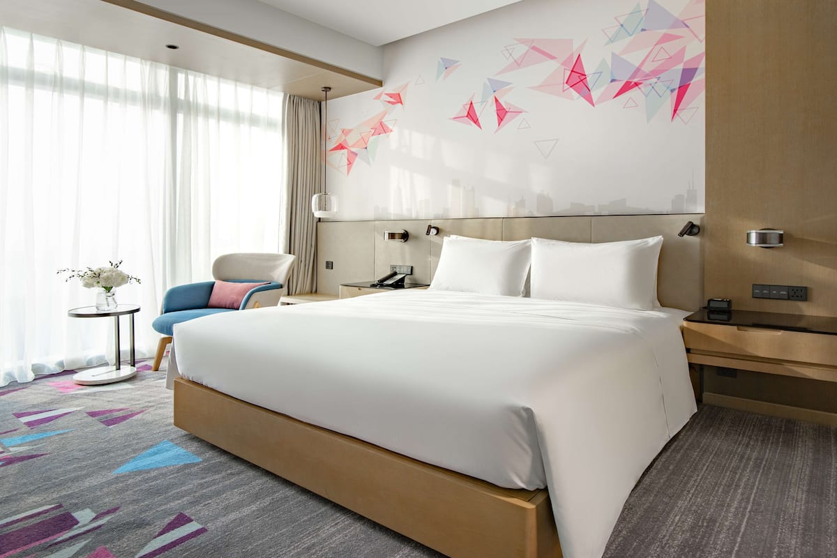 Een moderne hotelkamer met een groot bed, een bureau, een stoel en een stadsgezicht op de muur.