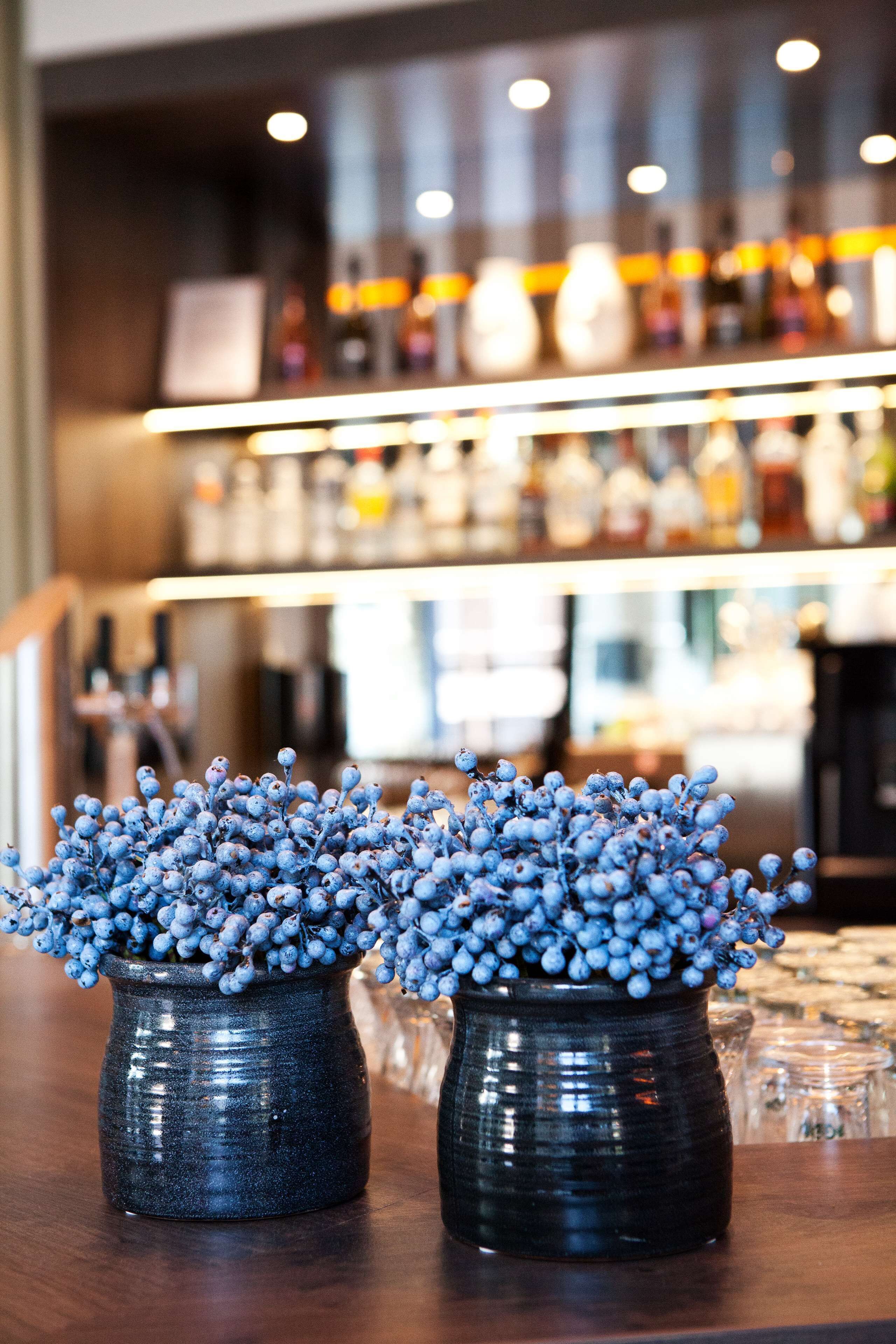 Two dark ceramic vases with blue berries on a wooden surface.