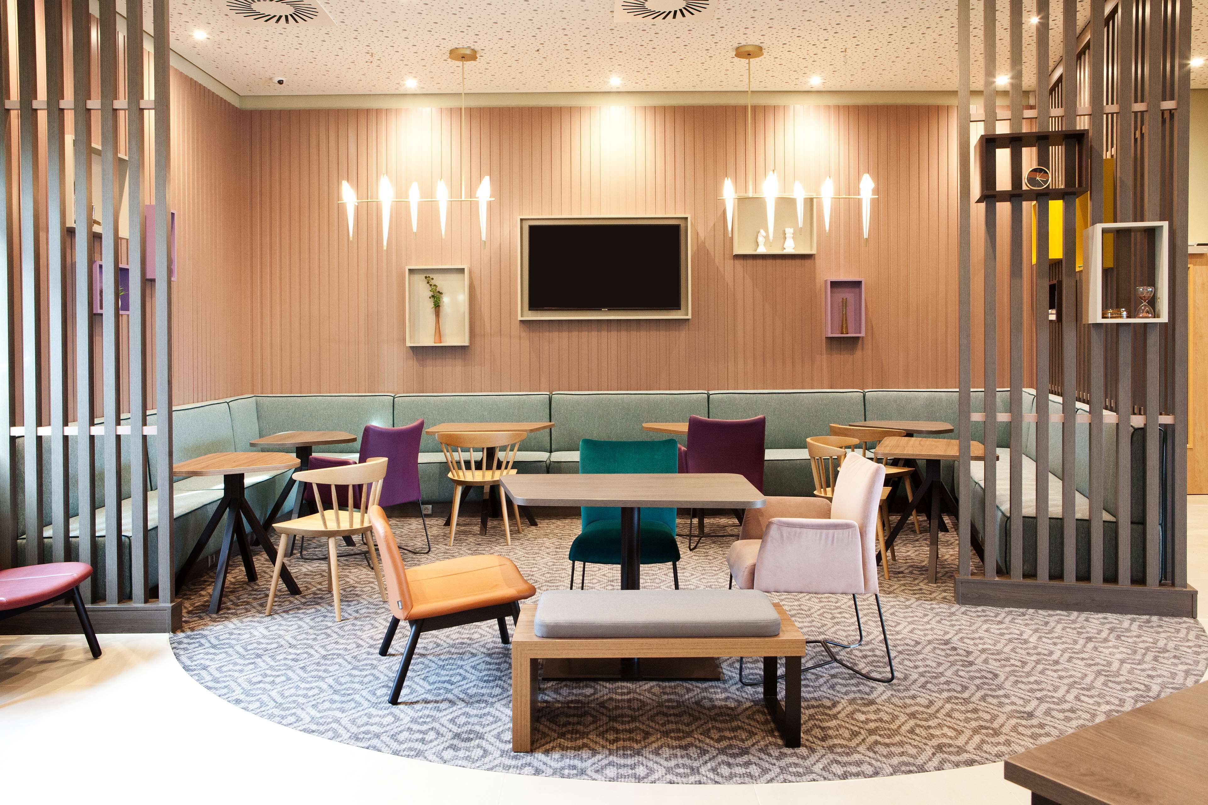 A modern restaurant with booths and tables, a large TV screen, and decorative lighting.