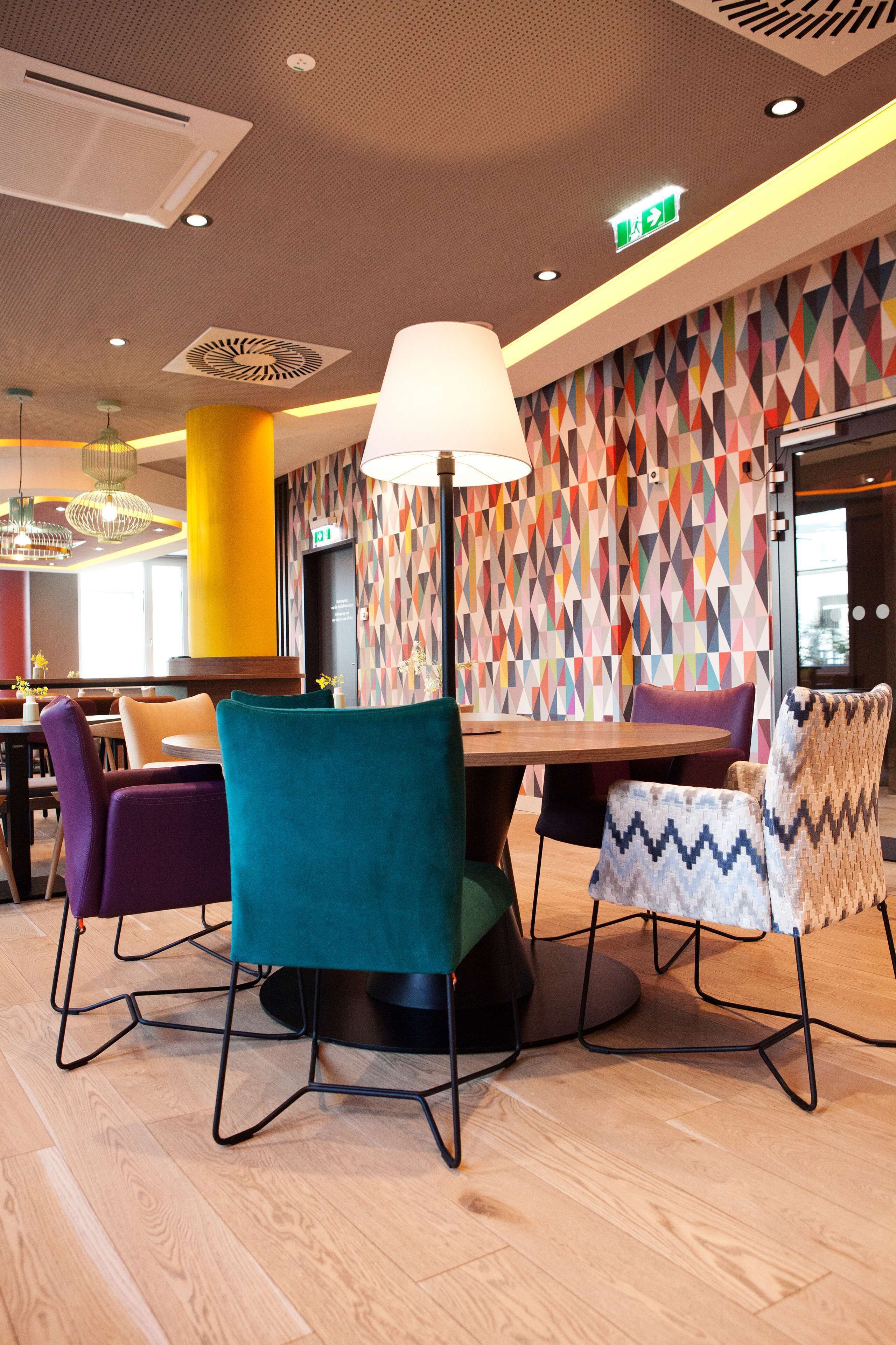 Un comedor moderno con una mesa redonda, sillas coloridas y un muro estampado.