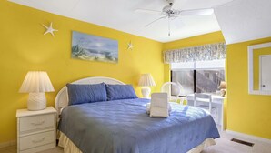 Een slaapkamer met een bed, twee nachtkastjes, een plafondventilator, een raam met gordijnen en een schilderij aan de muur.