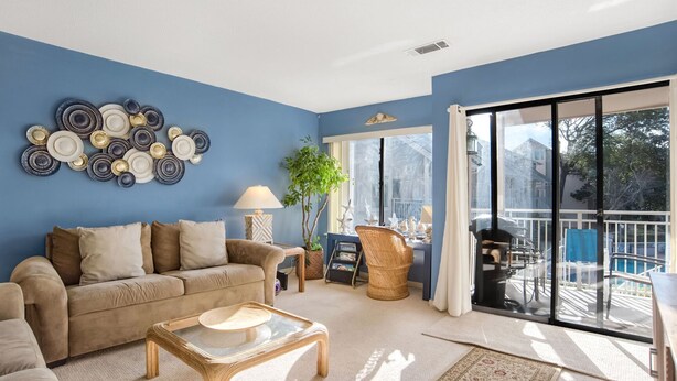 Een woonkamer met een blauwe wand, een bank, een bijzettafeltje, een lamp en een groot raam met uitzicht op een zwembad.
