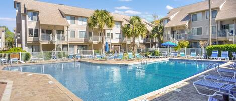 A swimming pool surrounded by lounge chairs and palm trees, with a brick walkway leading to the pool.