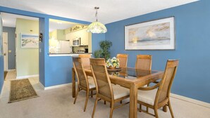 Een eetgedeelte met een houten tafel en stoelen, een hanglamp en een ingelijst schilderij aan de muur.