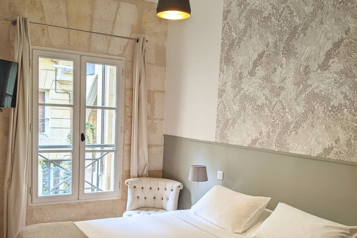 A bedroom with a large bed, a chair, a lamp, and a wall-mounted TV.