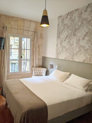 A bedroom with a large bed, a chair, a lamp, and a wall-mounted TV. - L' Apparthôtel Particulier Bordeaux (Bordeaux)
