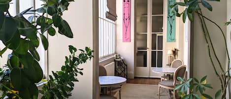 Una habitación acogedora con una mesa redonda y dos sillas, una ventana con vistas y una puerta con paneles de vidrio esmerilado.
