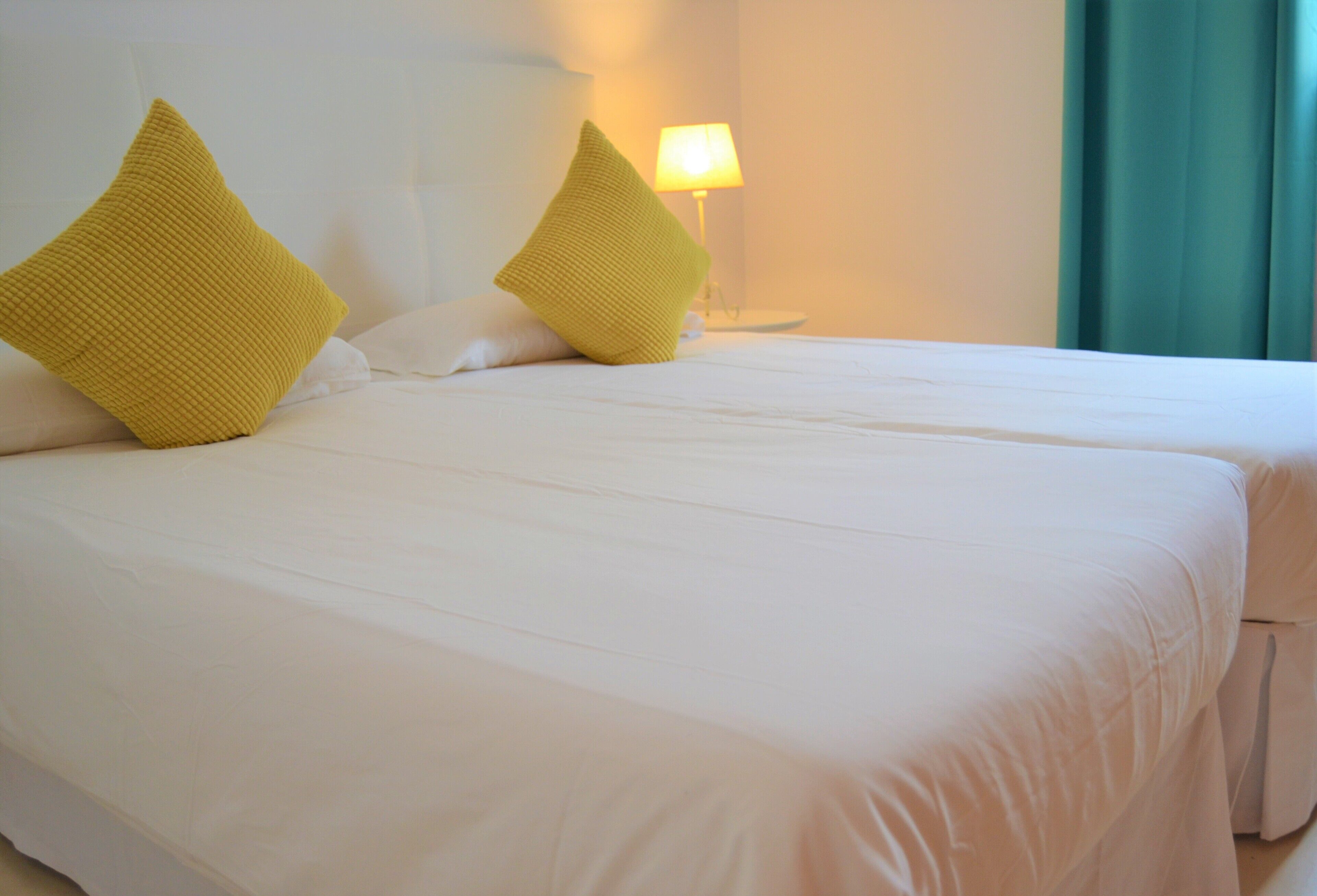 A hotel room with two beds, white bedding, and a lamp on a bedside table.