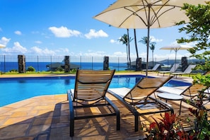 A poolside area with lounge chairs, umbrellas, and a view of the ocean.