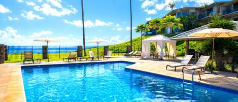 A swimming pool with lounge chairs and umbrellas, a stone fence, and a view of the ocean.