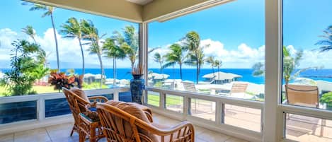 A room with a view of the ocean, a dining table with chairs, and a large vase.
