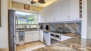 Una cocina moderna con armarios blancos, encimeras de granito, horno empotrado y ventilador de techo.