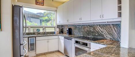 Una cocina moderna con armarios blancos, encimeras de granito, horno empotrado y ventilador de techo.