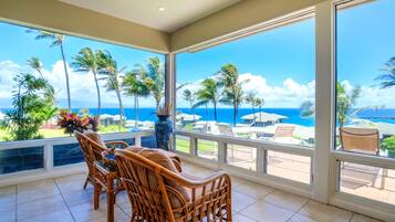 A room with a view of the ocean, a dining table with chairs, and a large vase.