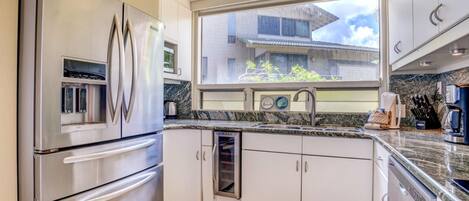 A modern kitchen with stainless steel appliances, a window with a view of buildings, and a granite countertop.