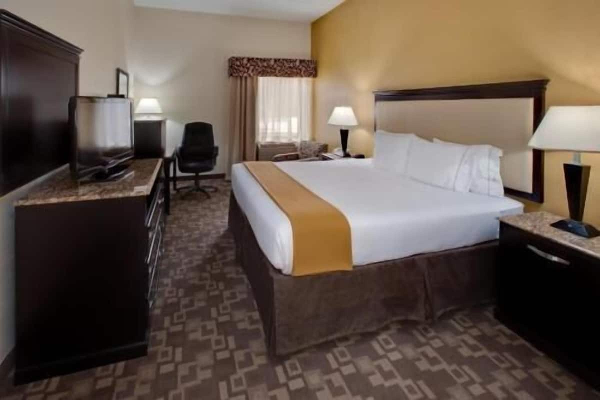 A hotel room with a large bed, a desk, a chair, and two bedside lamps.
