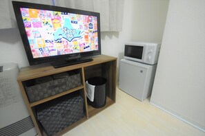 Compact living space with a television, microwave, and trash bin.