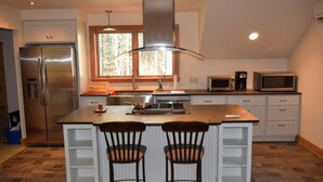 Moderni keittiö, jossa on keskeinen keittiösaareke, kaksi baarituolia, ruostumattomasta teräksestä valmistettu jääkaappi, mikroaaltouuni ja ikkuna, josta tulee luonnonvaloa.