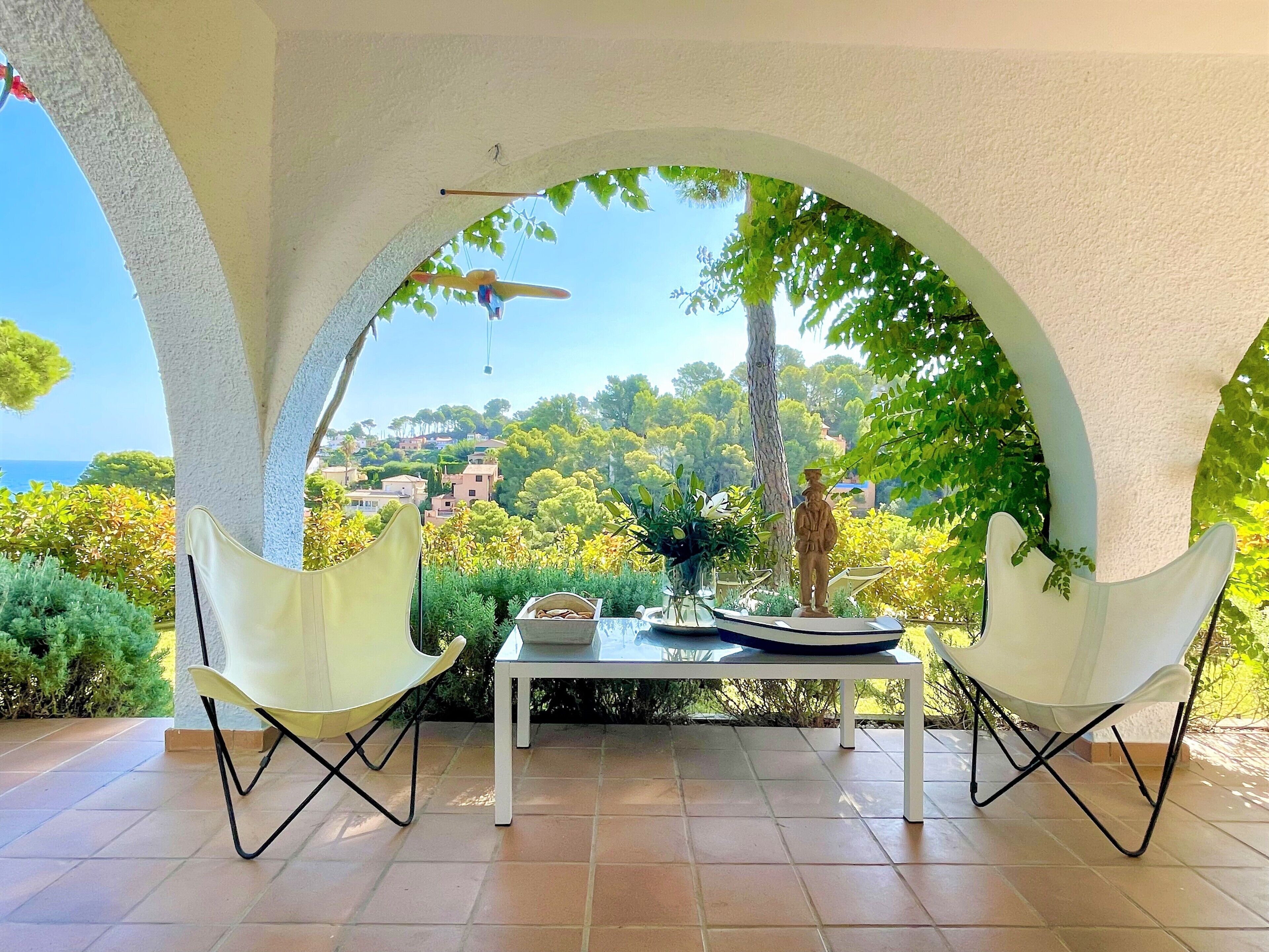 An outdoor patio with two white chairs, a table, and a view of a coastal town.