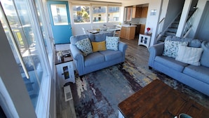 A modern living room with a blue sofa set, a wooden coffee table, and a view of the kitchen and balcony. - Oceanfront & Access, Epic Views & Sounds, Pool, Gated & easy Parking, Prime Spot (Monterey)