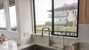 A modern kitchen with a large window, a stainless steel sink, and a marble countertop. - Oceanfront & Access, Epic Views & Sounds, Pool, Gated & easy Parking, Prime Spot (Monterey)
