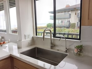 A modern kitchen with a large window, a stainless steel sink, and a marble countertop. - Oceanfront & Access, Epic Views & Sounds, Pool, Gated & easy Parking, Prime Spot (Monterey)