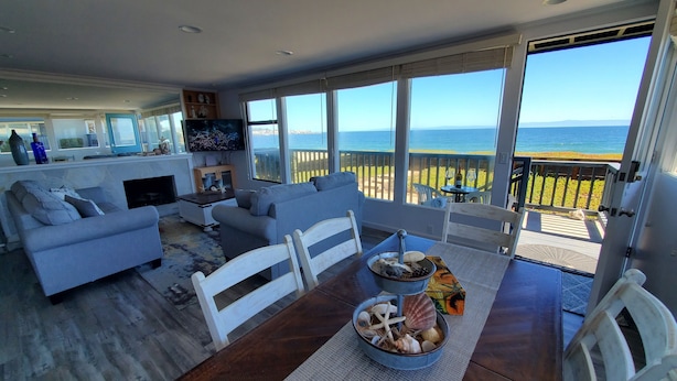A spacious living area with a large window overlooking the sea, a dining table with a centerpiece of seashells, and a cozy seating arrangement. - Oceanfront & Access, Epic Views & Sounds, Pool, Gated & easy Parking, Prime Spot (Monterey)