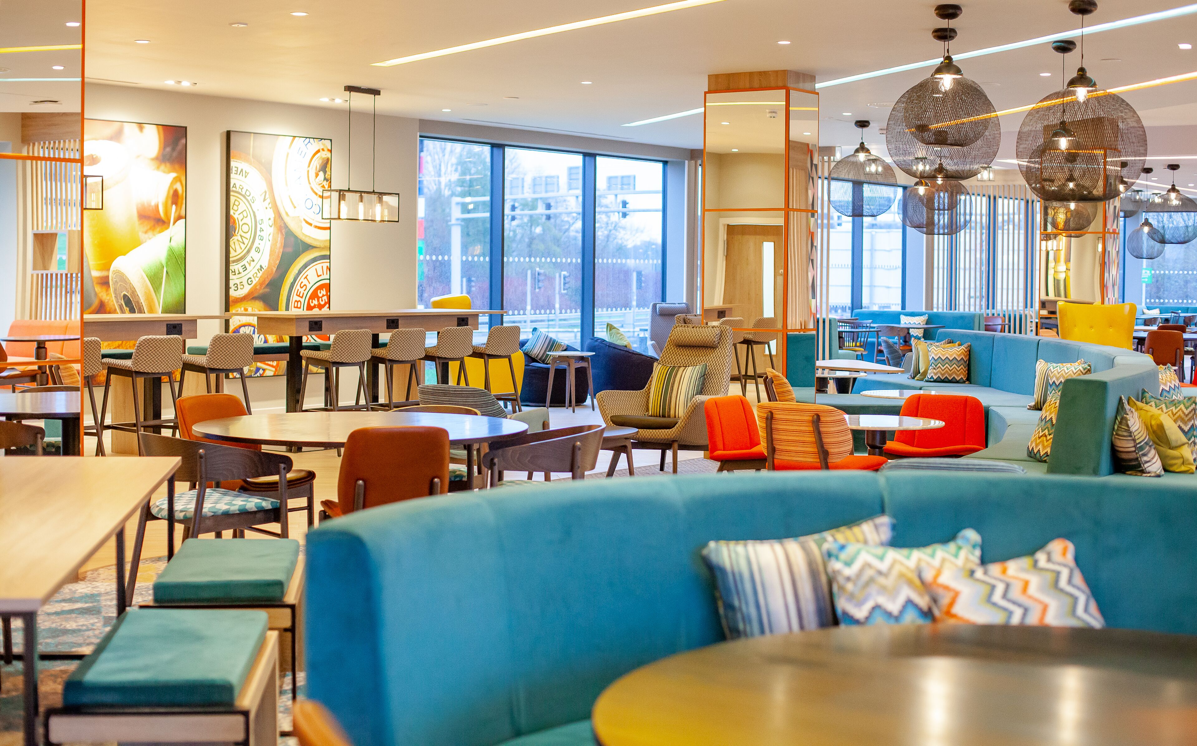 A modern dining area with multiple seating options, including tables and chairs, and a large blue sofa with colorful cushions.