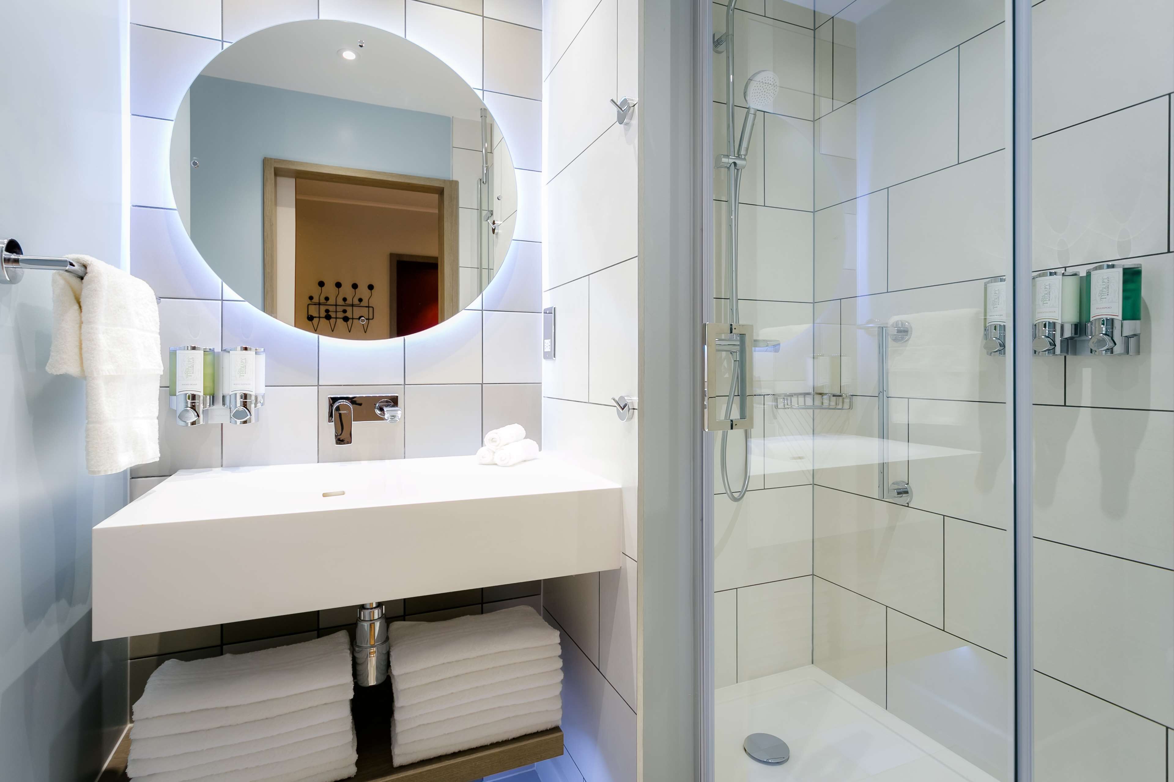 A modern bathroom with a white sink, a round mirror, and a glass-enclosed shower.