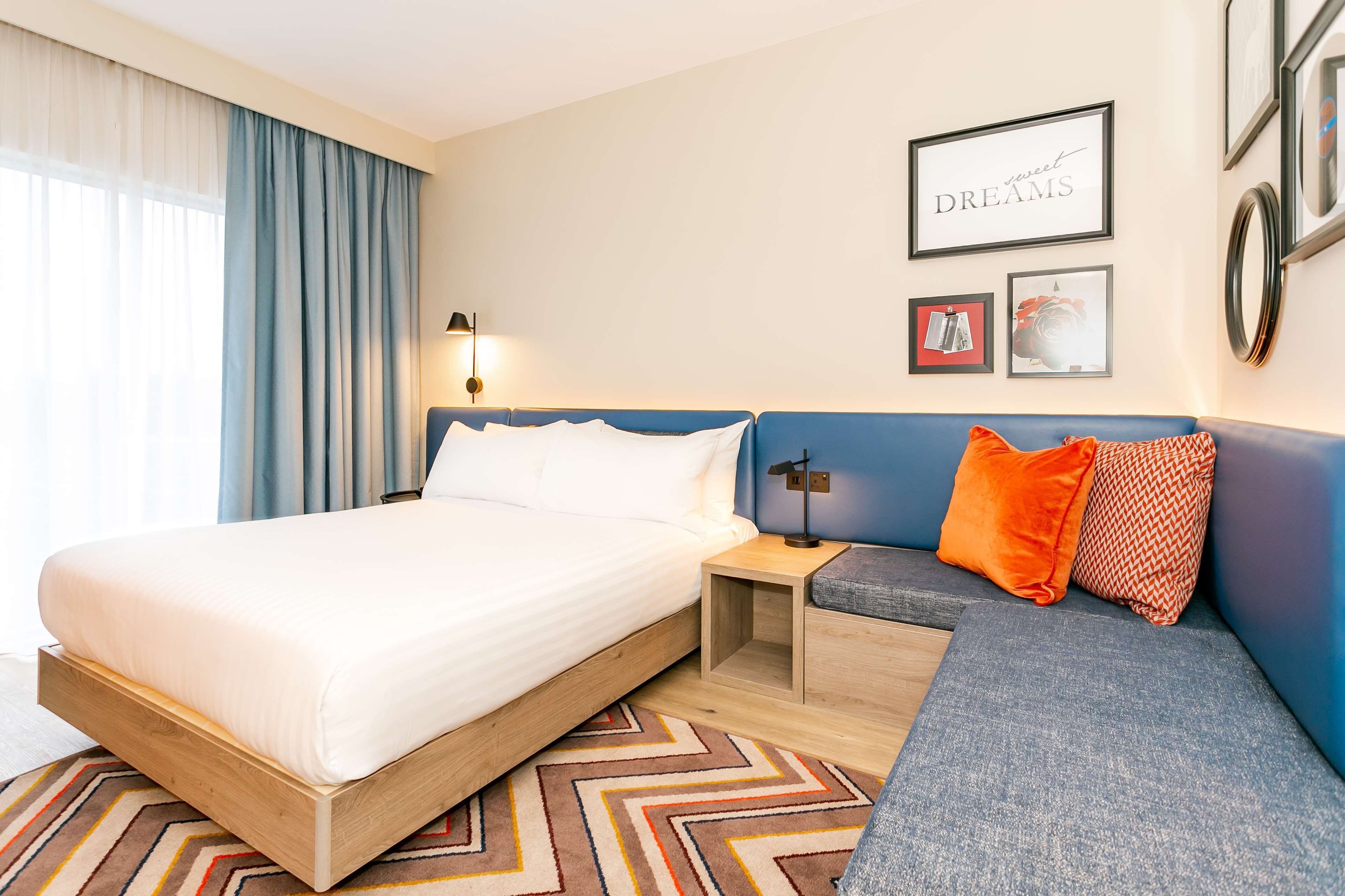 Una habitación de hotel con cama, mesita de noche, sofá y una pared decorada con cuadros.