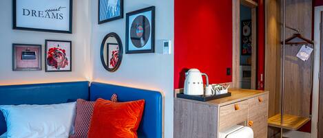 A hotel room with a bed, a dresser, and a kitchenette.