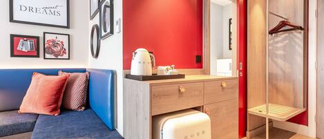 A modern room with a blue sofa, a white minibar, and a red accent wall.