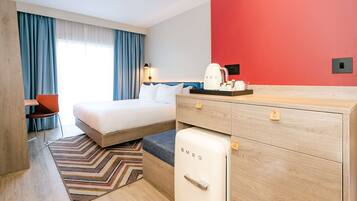 Habitació d'hotel moderna amb llit, escriptori, nevera i cafetera.
