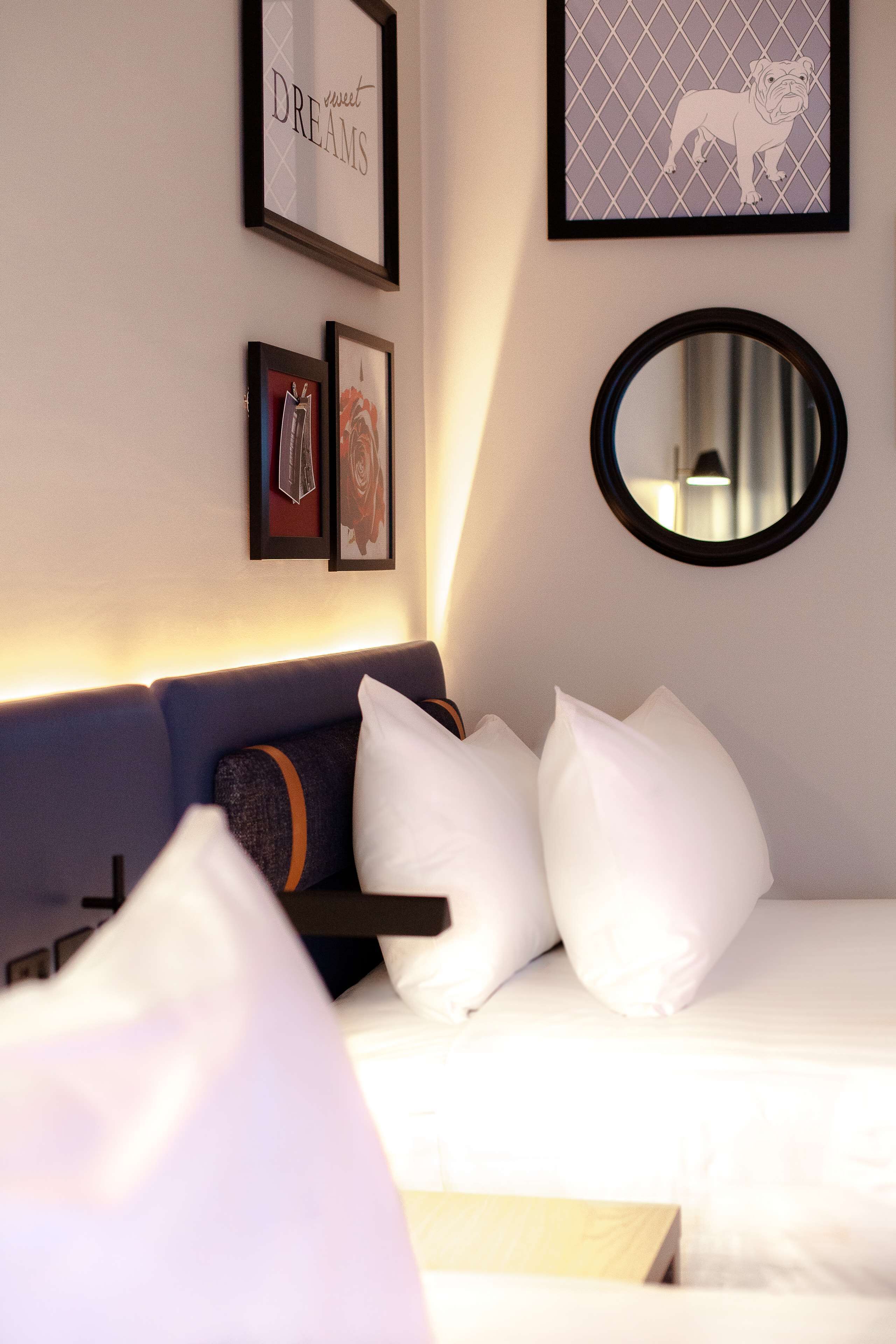 Habitación de hotel ordenada con cama, sofá, espejo y cuadros en la pared.
