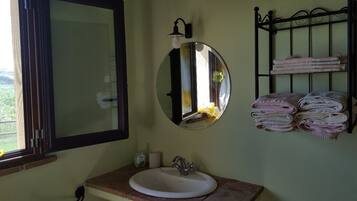 Une salle de bain avec un miroir rond, un lavabo et un porte-serviettes sur lequel sont pliées des serviettes.
