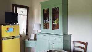 Une pièce avec un réfrigérateur jaune, un meuble vert, une table recouverte d’une nappe blanche et deux chaises en bois.