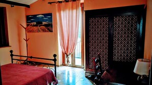 Une chambre à coucher avec un lit, une chaise, une table, une porte à motifs et un tableau accroché au mur.