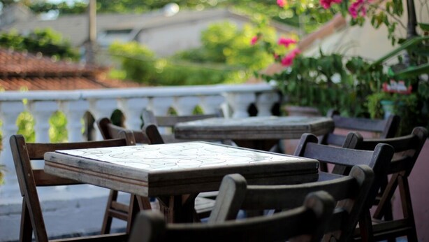 Outdoor seating with tables and chairs, surrounded by greenery and a white railing. - Aldeia Produções Hostel & Bar (Búzios)