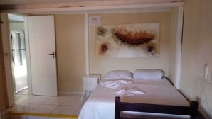 A bedroom with a bed, a nightstand, a wall-mounted painting, and a door leading to another room. - Aldeia Produções Hostel & Bar (Búzios)