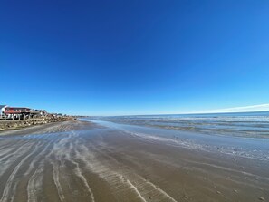A beach with a wooden pier and buildings on the left. - Gulf Views and good vibes! (Surfside Beach)