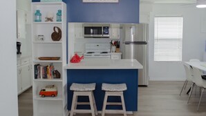 Une cuisine moderne avec un mur d’accent bleu, un panneau d’accueil, des meubles blancs et un petit îlot avec des tabourets.