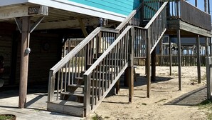 Un bâtiment turquoise doté d’une terrasse en bois et d’un escalier menant à une zone abritée.