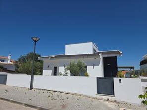 A modern two-story house with a white exterior, a black door, and a small garden area. - VILLA WITH 4 SUITES + 1, WALKING DISTANCE TO THE BEACH, SWIMMING POOL, AIR CONDITIONING, PARKING   (Carvalhal-GDL)